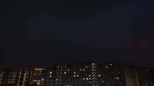Timelapse of dark clouds moving above illuminated apartment buildings in an urban residential district at night