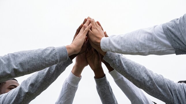 Diverse group of people showing unity and teamwork with hands stacked in a collective high-five gesture.
