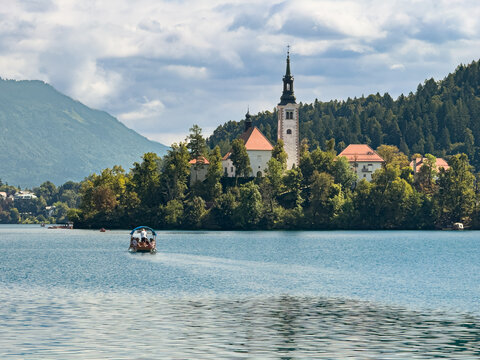 Traditional pletna boat sailing across Lake Bled toward the iconic island church surrounded by mountains and dramatic clouds in Slovenia