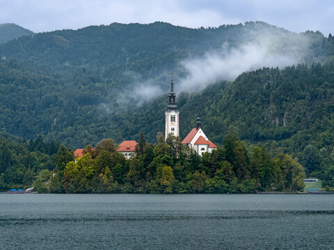 Bled Island with the Church of the Assumption surrounded by Lake Bled and misty forested mountains after summer rain