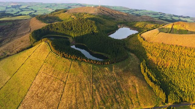 Aerial view of the Sete Cidades volcanic crater lakes surrounded by lush green slopes and dense forest under golden hour light in Sete Cidades, Azores, Portugal.