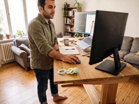 Nahaufnahme einer bunten Babyrassel neben der Computermaus am Stehschreibtisch im Homeoffice eines Mannes