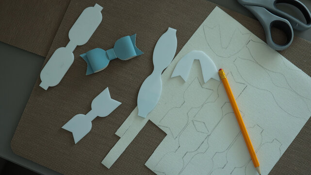 Crafting workspace with paper bow cutouts scissors and pencil for handmade DIY decoration project. JPG