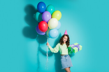 Obraz premium Young woman celebrating a colorful birthday with balloons and gift wearing a party hat against a turquoise background