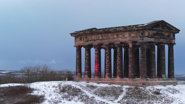 Aerial drone shot rising behind the iconic Penshaw Monument on a snow-covered hill in Sunderland during a cold winter day.