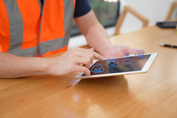 Construction worker wearing a high-visibility safety vest using a digital tablet with cloud computing icons. Technology, digital workflow, data management, and construction industry concept. © Teelapon