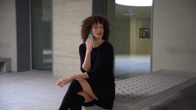 A stylish woman in an elegant black dress confidently seats in a modern architectural space