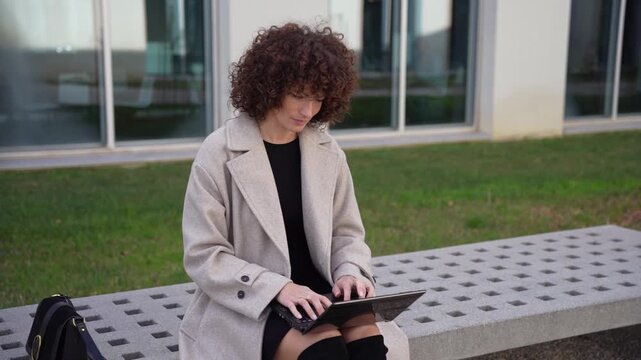 A Professional Woman is Working Exclusively Outdoors with her Laptop in a Modern Cityscape
