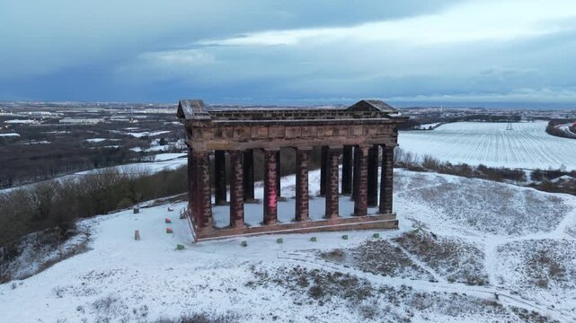 Telephoto drone orbit shot around the snow-covered Penshaw Monument in Sunderland, revealing the wider Wearside city skyline in the background.