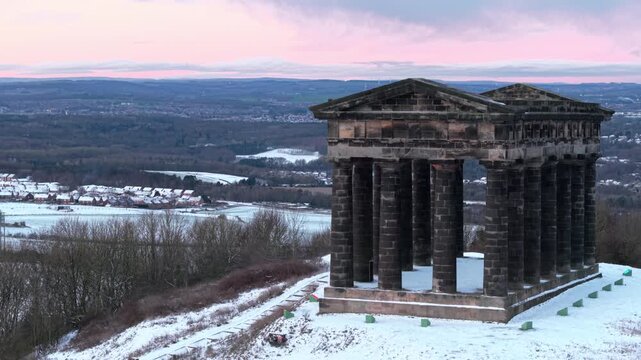 Aerial drone shot pulling back slowly from Penshaw Monument in Sunderland during a snow-covered winter sunrise revealing the County Durham landscape in the background.