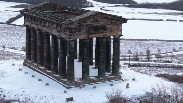 Telephoto aerial tracking shot rising over the imposing columns of Penshaw Monument in Sunderland with a snow-covered countryside background