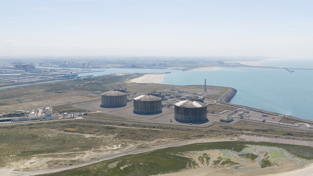 Aerial view of the Dunkirk LNG Terminal featuring three large storage tanks situated on the coast near industrial port infrastructure in Loon-Plage, Hauts-de-France, France.