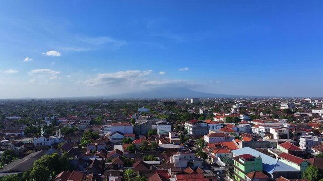 Aerial view of Jalan Jogokaryan, featuring dense residential rooftops and a distant mountain under a clear blue sky in Kecamatan Mantrijeron, Daerah Istimewa Yogya, Indonesia.
