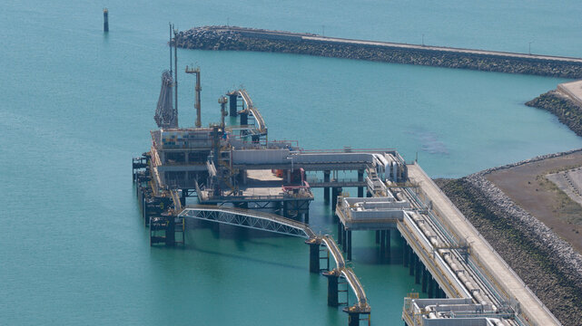 Aerial view of Dunkirk LNG Terminal featuring industrial infrastructure, pipelines, and loading platforms extending into the turquoise waters of the North Sea in Loon-Plage, France.