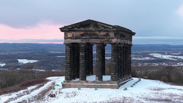 Slow drone orbit shot of the snow-covered Penshaw Monument in Sunderland during twilight, featuring the rolling County Durham landscape in the background.