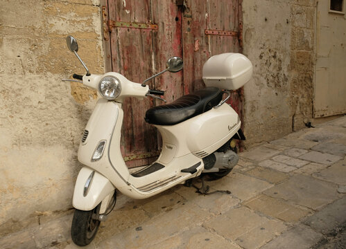 Vintage white Vespa scooter parked against the background of a shabby wall in a narrow European street in Valletta, Malta - March, 2026.