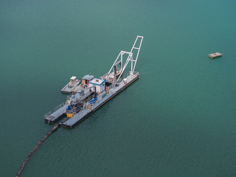 Aerial view of a dredger vessel operating on calm green water with a long suction pipe extending into the depths in the Netherlands.