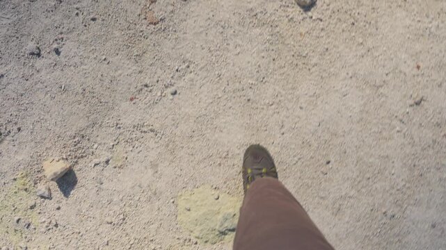 Personal perspective of a hiker wearing trekking boots walking on the volcanic, sulfur rich soil of Mount Io in Akan Mashu National Park, Hokkaido, Japan, during a sunny day
