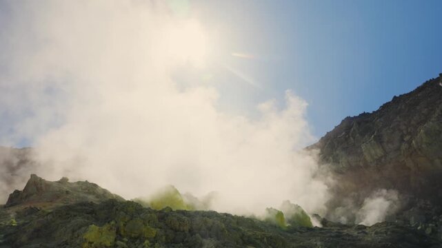 Volcanic gas and steam rising from sulfurous fumaroles on a barren mountainside in Akan Mashu National Park, Hokkaido, against a bright, sunny blue sky, showcasing geothermal activity
