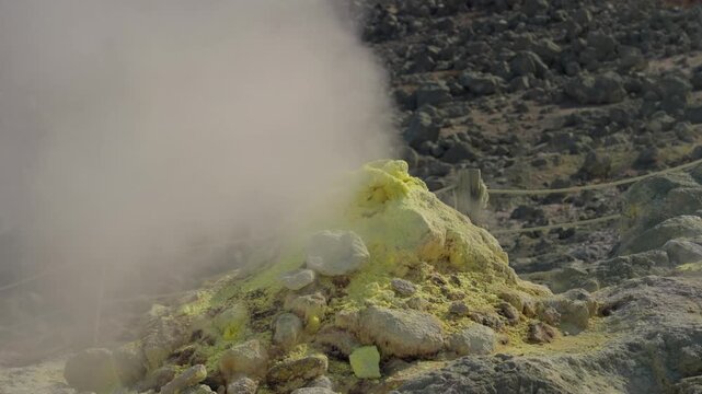 Volcanic gas and steam venting from a fumarole in the geothermal area of Akan Mashu National Park in Hokkaido, Japan, releasing sulfur deposits on the rocky, arid landscape