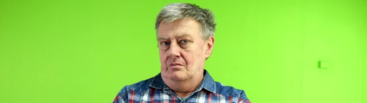 Mature man with gray hair having a serious expression wearing a plaid shirt his face showing no as denial rejection on a green backdrop.
