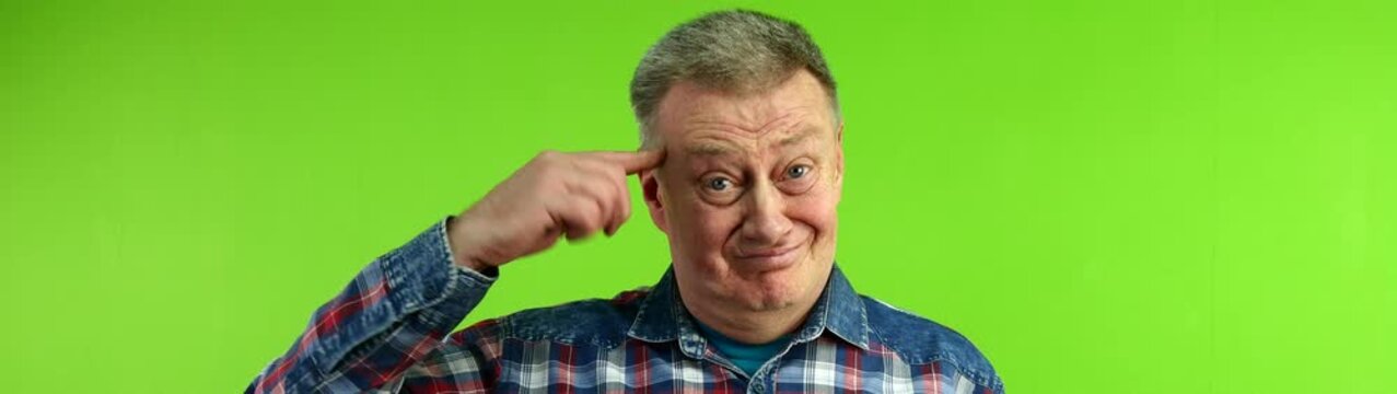 Mature man pointing finger to temple conveying showing fool problem solving and having a good idea on a green screen.