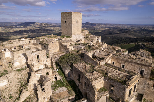 Aerial view of the abandoned Craco Historical Center with its iconic medieval tower surrounded by ruined stone buildings and rugged landscape in Craco, Basilicata, Italy.