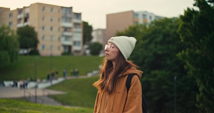 Side profile portrait of a woman wearing a beanie and backpack in a
green urban park. Soft natural light and a blurred city background create a relaxed outdoor lifestyle scene.