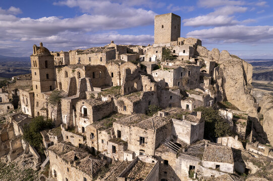 Aerial view of the abandoned Craco Historical Center, featuring ruined stone buildings, a bell tower, and a central tower atop a rocky hill in Craco, Basilicata, Italy.