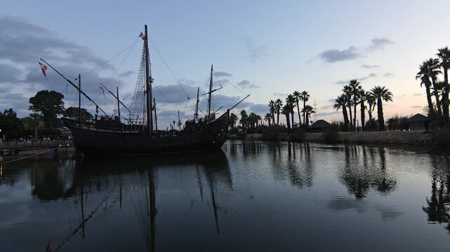 Cinematic wide shot of the historical replica ships. Pinta, Ni&ntilde;a and Santa Mar&iacute;a docked at Muelle de las Carabelas during a serene sunset. Located in La Rabida, Palos de la Frontera, Huelva, Spain.