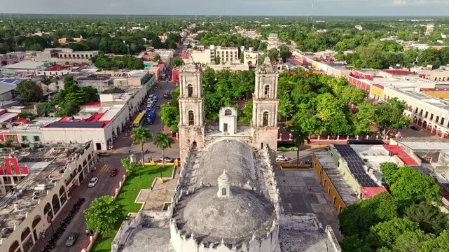 Aerial view of the San Gervasio Cathedral and its plaza in Valladolid, Mexico, tree-filled gardens and colonial buildings framing the historic square.