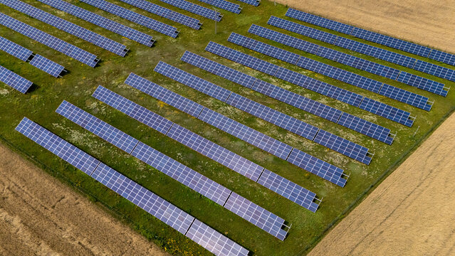 Aerial view of a large solar farm with rows of photovoltaic panels installed on green grassy fields surrounded by agricultural land in Grudziadz, Kuyavian-Pomeranian, Poland.