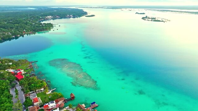 Aerial view of the turquoise Bacalar lagoon and its lakeside town, Mexico, pale reefs and deep blue channels patterning the water along the shore.
