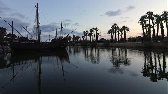 Cinematic wide shot of the historical replica ships. Pinta, Ni&ntilde;a and Santa Mar&iacute;a docked at Muelle de las Carabelas during a serene sunset. Located in La Rabida, Palos de la Frontera, Huelva, Spain. 