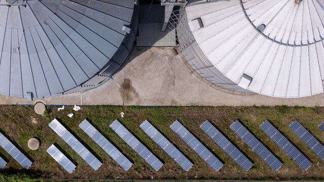 Aerial view of industrial grain silos and rows of solar panels installed in a grassy field in Grudziadz, Kuyavian-Pomeranian, Poland.
