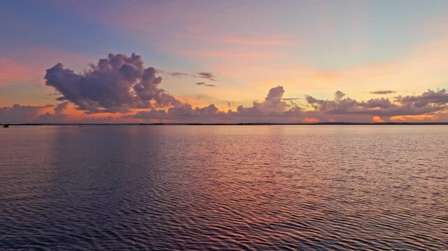 Aerial view at dusk over the calm Bacalar lagoon, Mexico, a single dramatic cloud and soft twilight glow reflected on the still water surface.