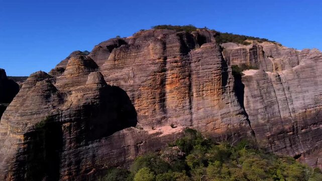 Drone camera orbiting a towering sandstone cliff showing ancient geological layers and green forest at the base in Serra da Capivara, Brazil.