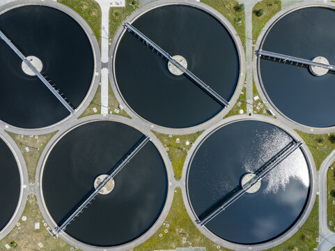 Aerial view of circular sedimentation tanks at a wastewater treatment plant with concrete walkways and surrounding green space in Munich, Bavaria, Germany.