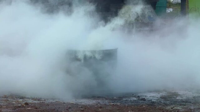 Person spraying fire extinguisher onto burning drum with thick smoke. Fire safety training, emergency, and firefighting concept footage.