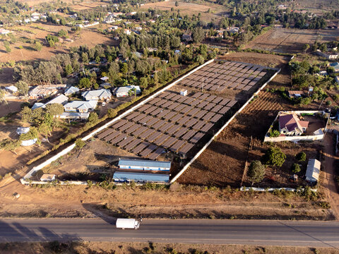 Aerial view of a solar panel array situated within a fenced compound near residential houses and a road in Loitokitok, Kajiado County, Kenya.