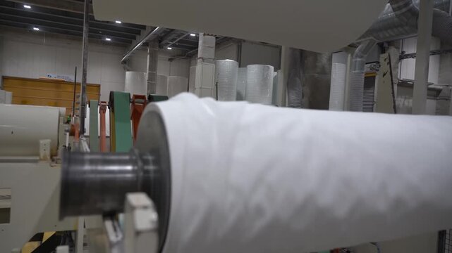 Large jumbo roll of white tissue paper winding on a rolling machine in a paper factory