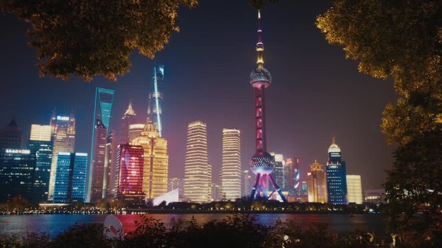 The illuminated Pudong skyline glows at night in Shanghai, framed by tree branches, with the colorfully lit Oriental Pearl Tower and surrounding skyscrapers reflecting off the Huangpu River.
