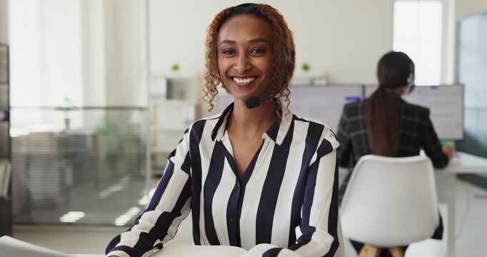 Woman operator with headset greets call service. Friendly agent offers support in a bright office, assisting clients via phone and chat with billing and tech issues. Positive customer concept.