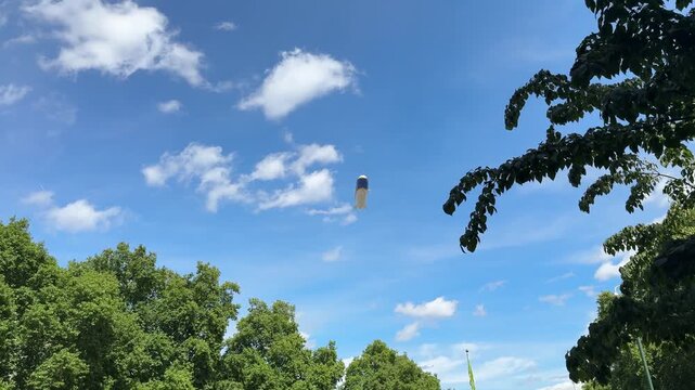 A blimp floats in a bright blue sky above green trees in London, England