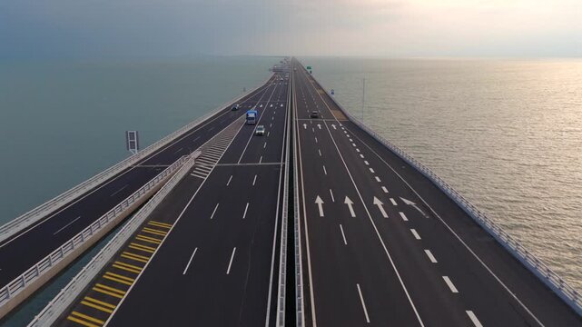 Aerial drone view of Qingdao Bay Cross-sea Bridge during blue hour dusk, heavy cargo and container trucks driving on marine viaduct, grand Chinese transportation infrastructure