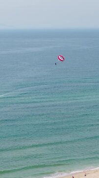 Aerial view of parasailing at My Khe Beach in Da Nang, Vietnam, showing a person flying above the ocean - drone, vertical shot