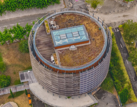 Aerial view of a modern circular office building with a green roof, rooftop garden, glass skylight, and integrated solar panels in Valence, Auvergne-Rhone-Alpes, France.