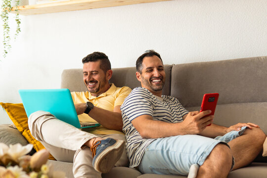 Gay couple laughing and using digital devices at home