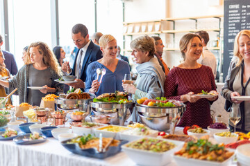 Fototapeta premium Diverse group enjoying a buffet at a social event in a bright setting.