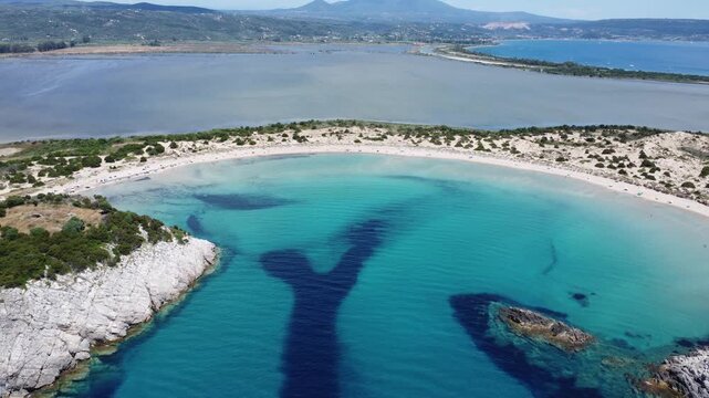 Drone view of the iconic Voidokilia Beach in Messinia, Greece, featuring a semicircular sandy bay, turquoise waters, coastal dunes, and pristine Mediterranean scenery.